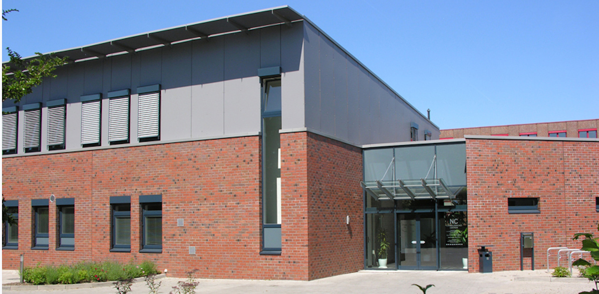 Modernes, zweigeschossiges Gebäude mit Glasfront und roten Ziegeln.