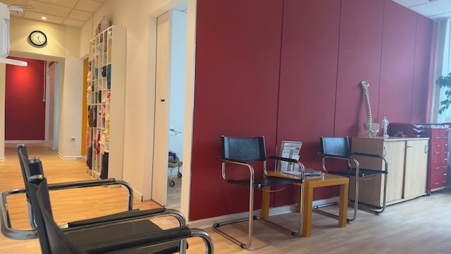 Eine Therapeutin untersucht den oberen Rücken und Nacken einer Frau, die über Schmerzen klagt und ihre Hände an den Nacken legt.